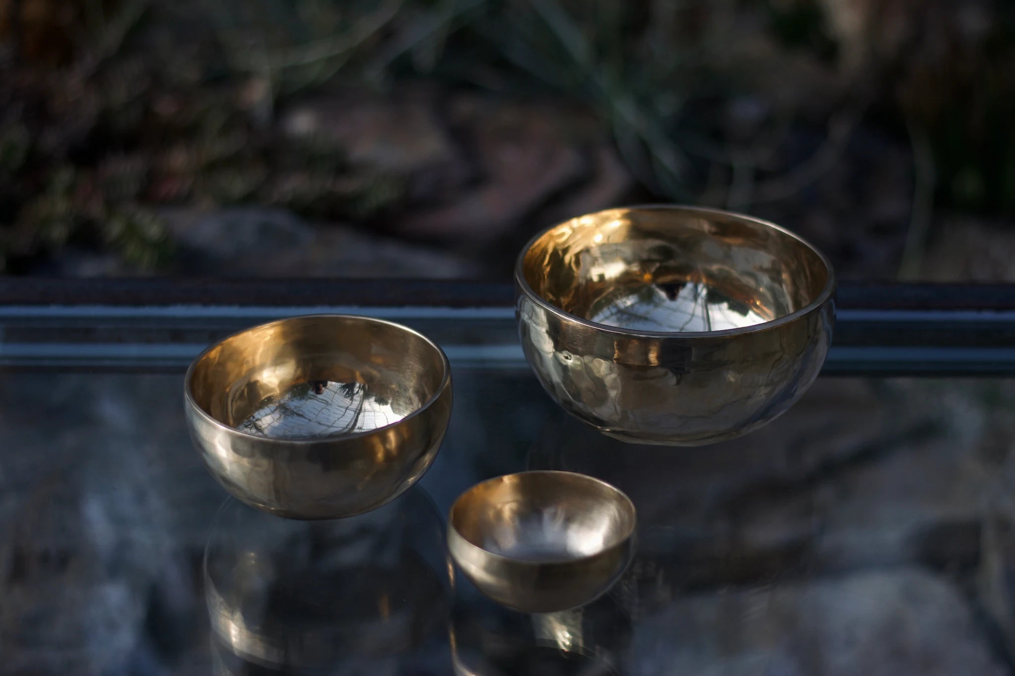 3er-Set Klangschalen von Sonner Sound spiegeln sich auf einem Glastisch. 