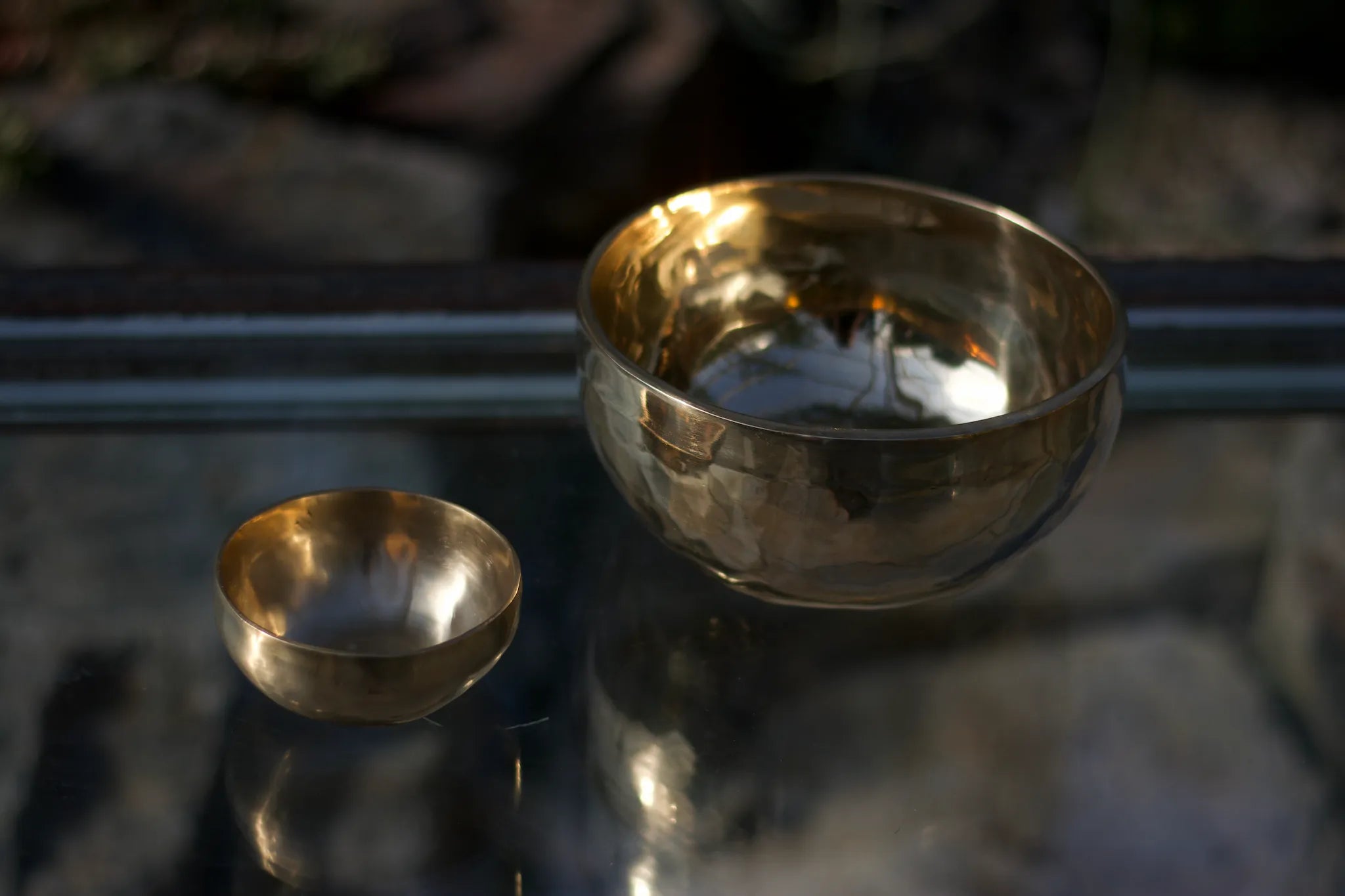 Zwei Klangschalen stehen auf einem Glastisch und spiegeln sich darin.
